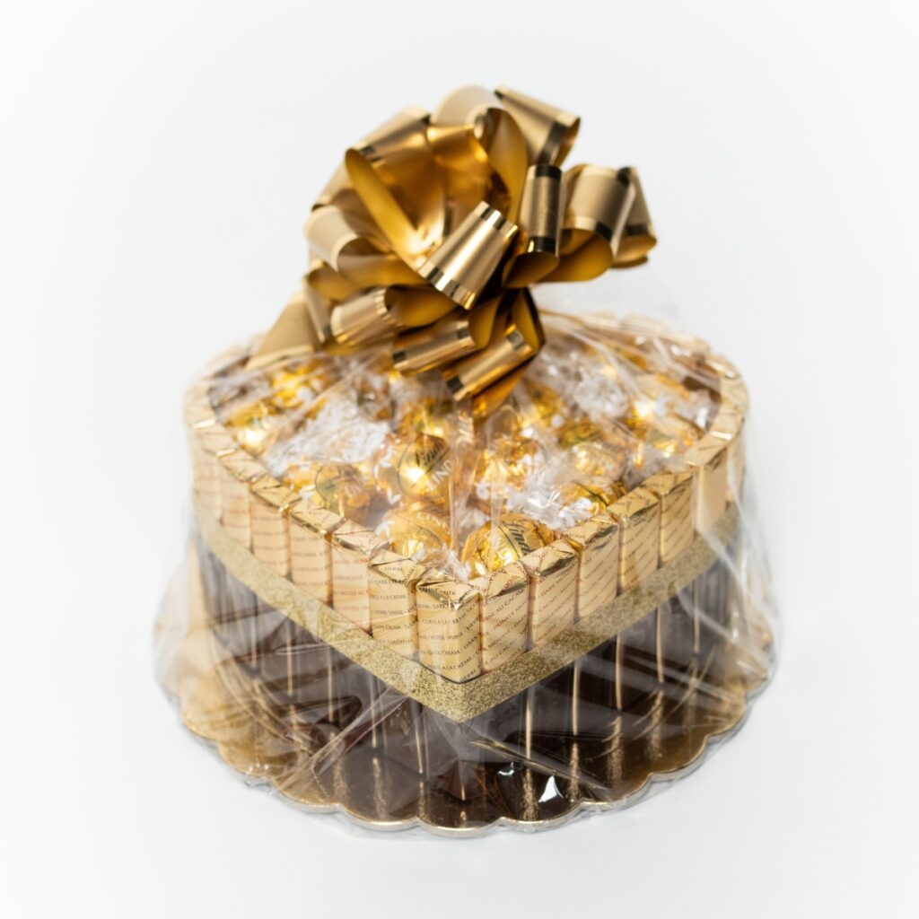 Darčekový kôš srdce s pralinkami Lindor a čokoládami Merci, zlatá stuha, biele pozadie.